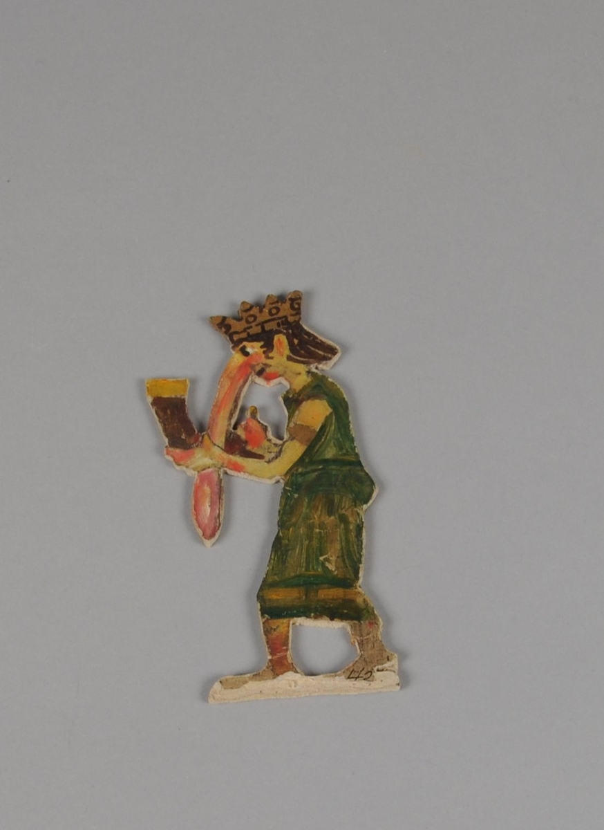 Figur av papp. Forestiller stående trolldame med stor nese og drikkehorn. Figuren er malt på begge sider.