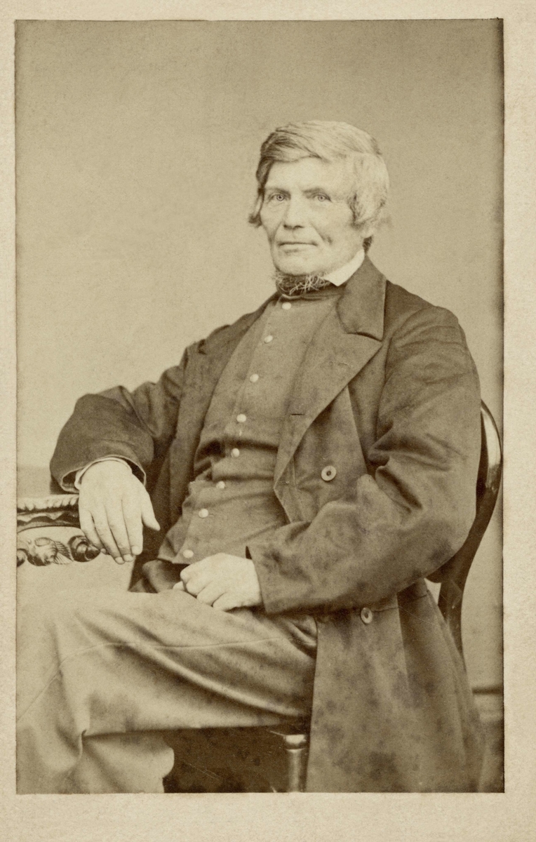 En man sitter vid ett bord, klädd i rock och väst