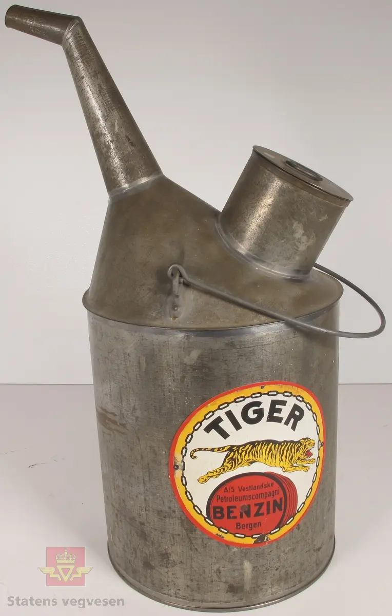 Sylinderformet kanne i metall med helletut, bærehåndtak og påfyllingshull med lokk. På kannen er det et sirkelformet merke med en tiger og påskriften A/S Vestlandske Petroleumscompagni TIGER BENZIN.