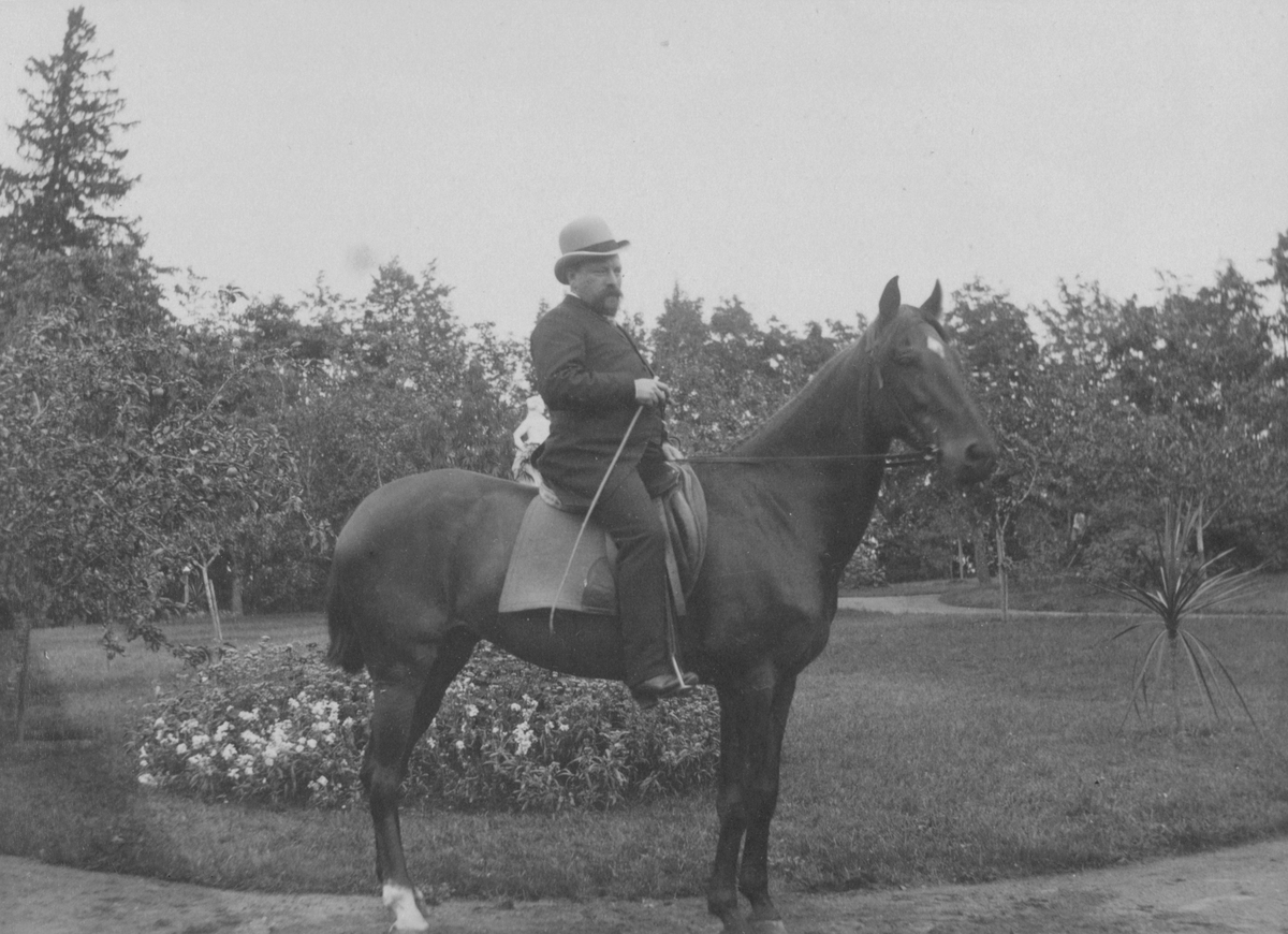 John Rettig till häst framför trädgårdplanteringar, sannolikt vid Villa Rettig, Gävle.