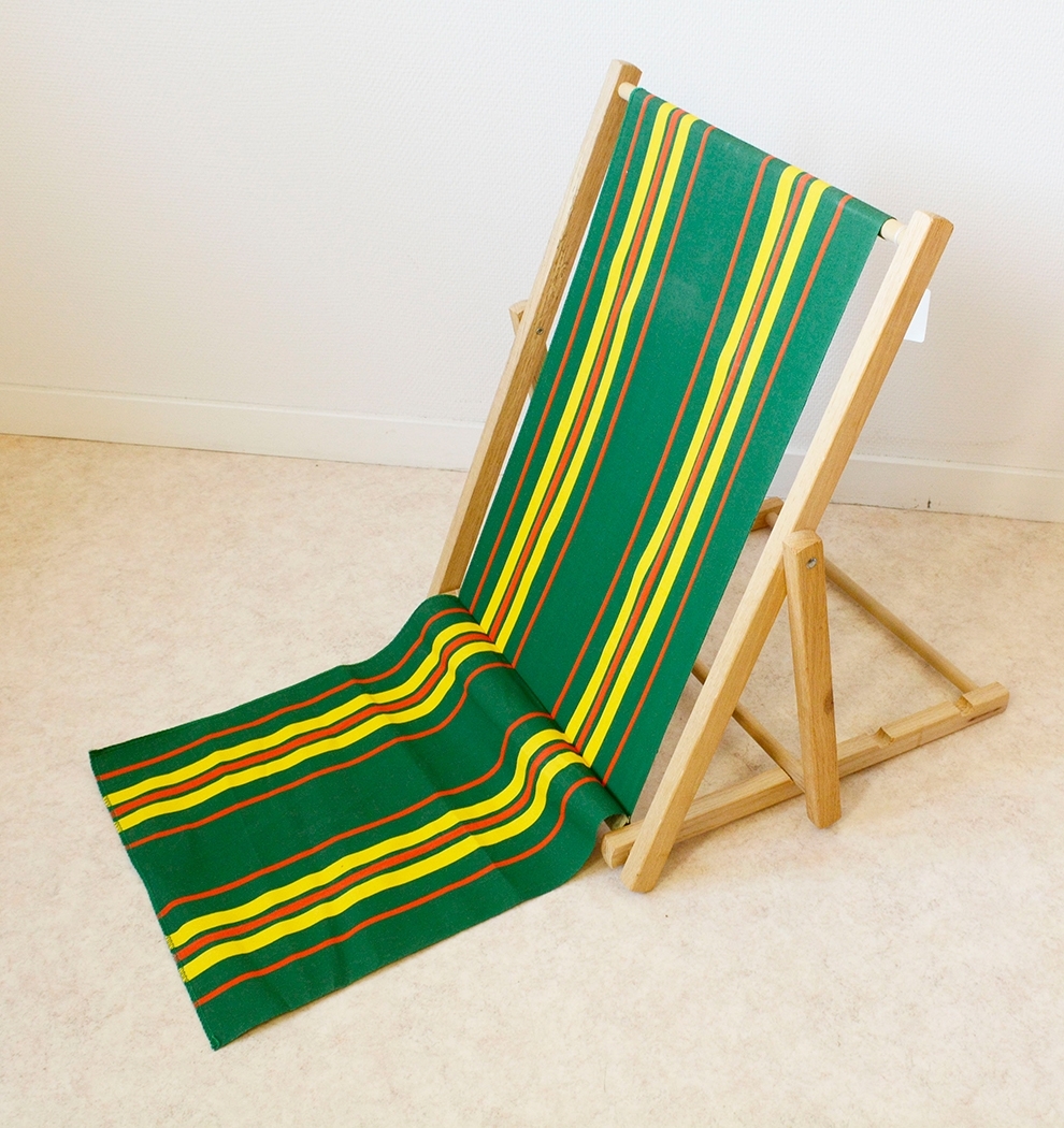 Strandstol med stomme i trä. Stommen klädd med markisväv i färgerna grön, gult och rött. Tyget nedtill är löst hängande och är avsett att sitta på, direkt på marken. Ryggen lutar man mot ryggstödet, vilket går att reglera lutningen på med hjälp av spåren i ramen.

Stommen har ramkonstruktion där två ramar är ihopsatta med genomgående rundstav i nederkanten.

Strandstolens modell och tyg är typiskt för 1960-talet.