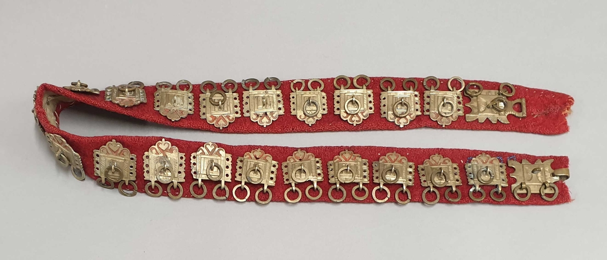 Belte av rød ull, med 20 metallstøler og beltespenner i hver ende.