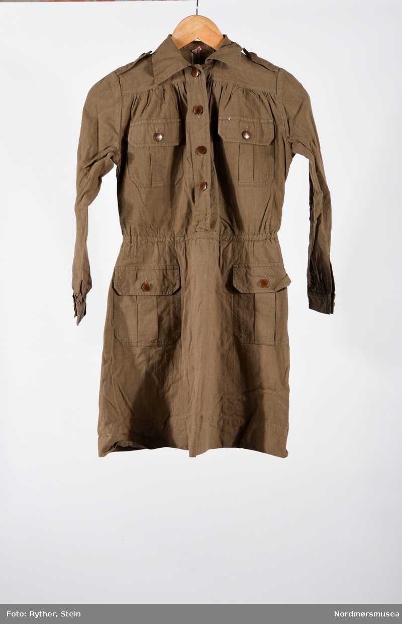Brun jakkekjole med brunt skinnbelte og gult skjerf til bruk for jentespeiderne i KFUK 1959 (Kristelig ungdomsorganisasjon). Beltet har to metallhemper, sannsynligvis for feste av speiderkniv mm.
