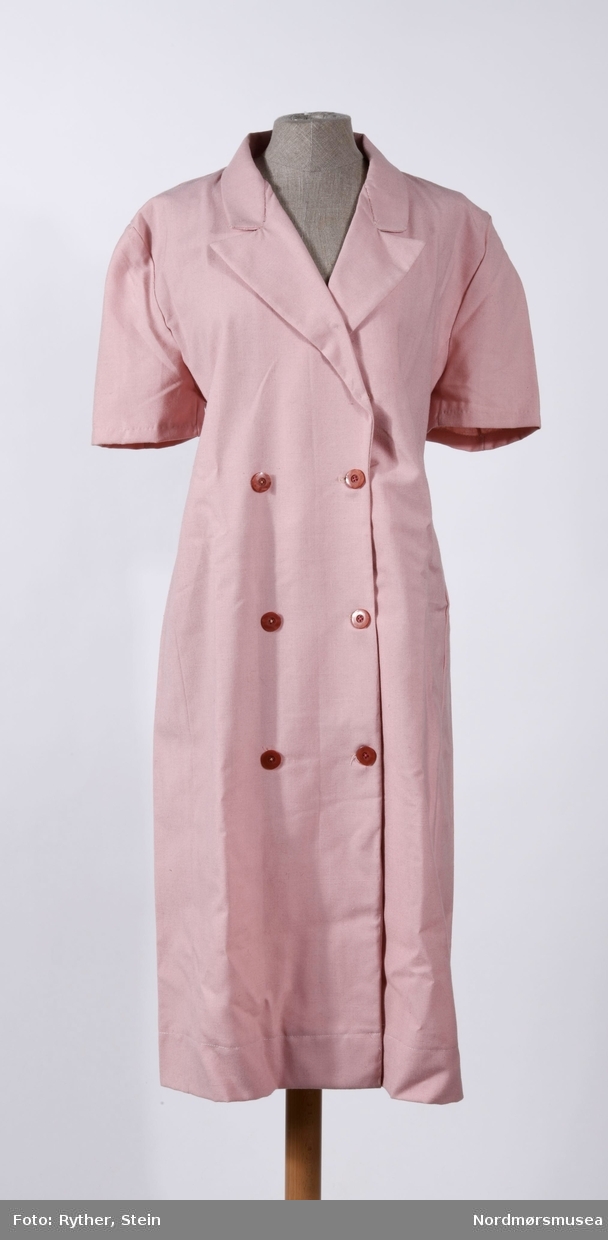 Rosa kjoleforkle med to dobbeltrader med knapper. Medfølger en liten plastpose på 19x22cm med ekstra stoff.