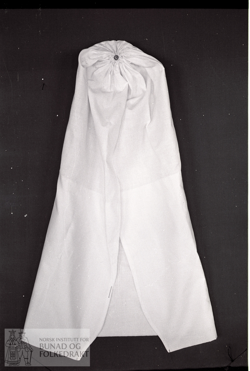 Nordhordlandsmessa 1974 - - - - - Tynt kvitt bomullslerret. L. til knute: 65 cm. L. forkant: 65 cm. Maskinsydd. Knuten sydd med rødt og hvitt bomullsgarn.