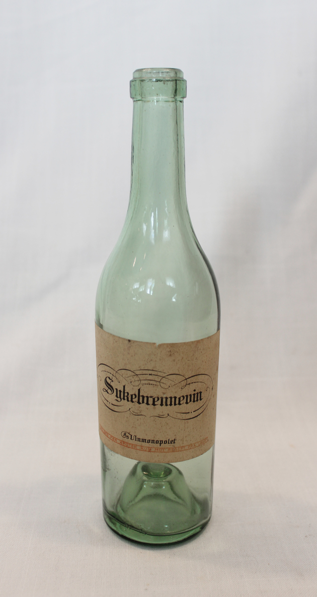 Grønn halvflaske med etikett med påskrift: "Sykebrennevin, Vinmonopolet A/S. Selges fra apotek kun mot resept fra lege".