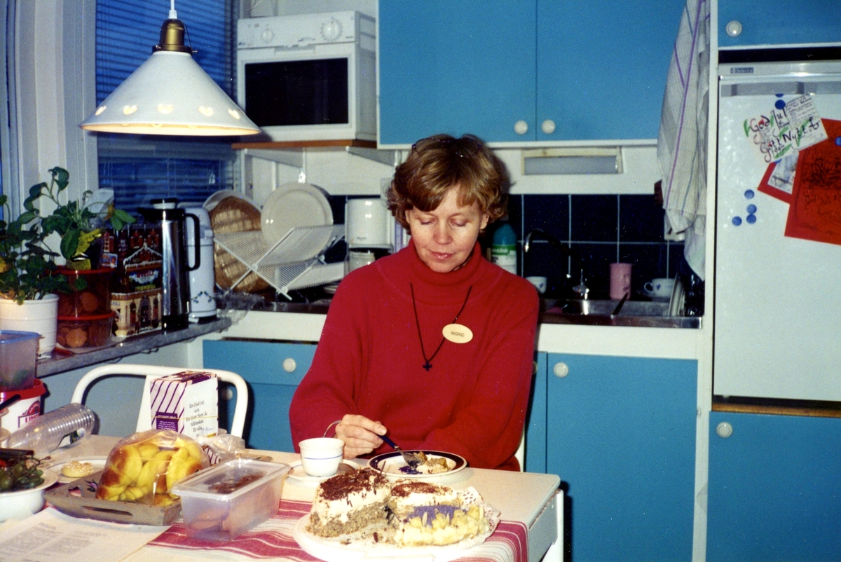 Biblioteksassistent Ingrid Hansson har rast i Kållered biblioteks personalrum (köket) 1990-tal. Hon dricker kaffe och äter tårta. Köksluckorna i bakgrunden är klarblå.