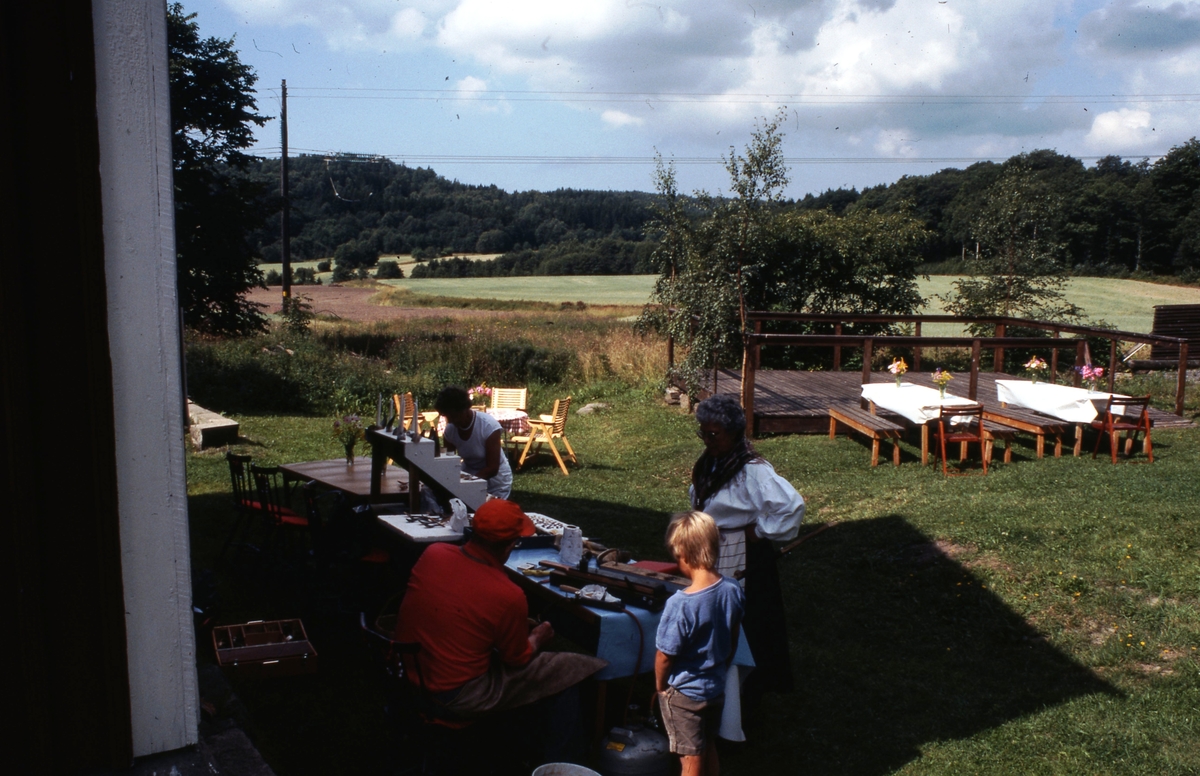 Besökare utanför Långåker Hembygdsgård år 1985. I bakgrunden ses uppdukade bord samt åkermark.