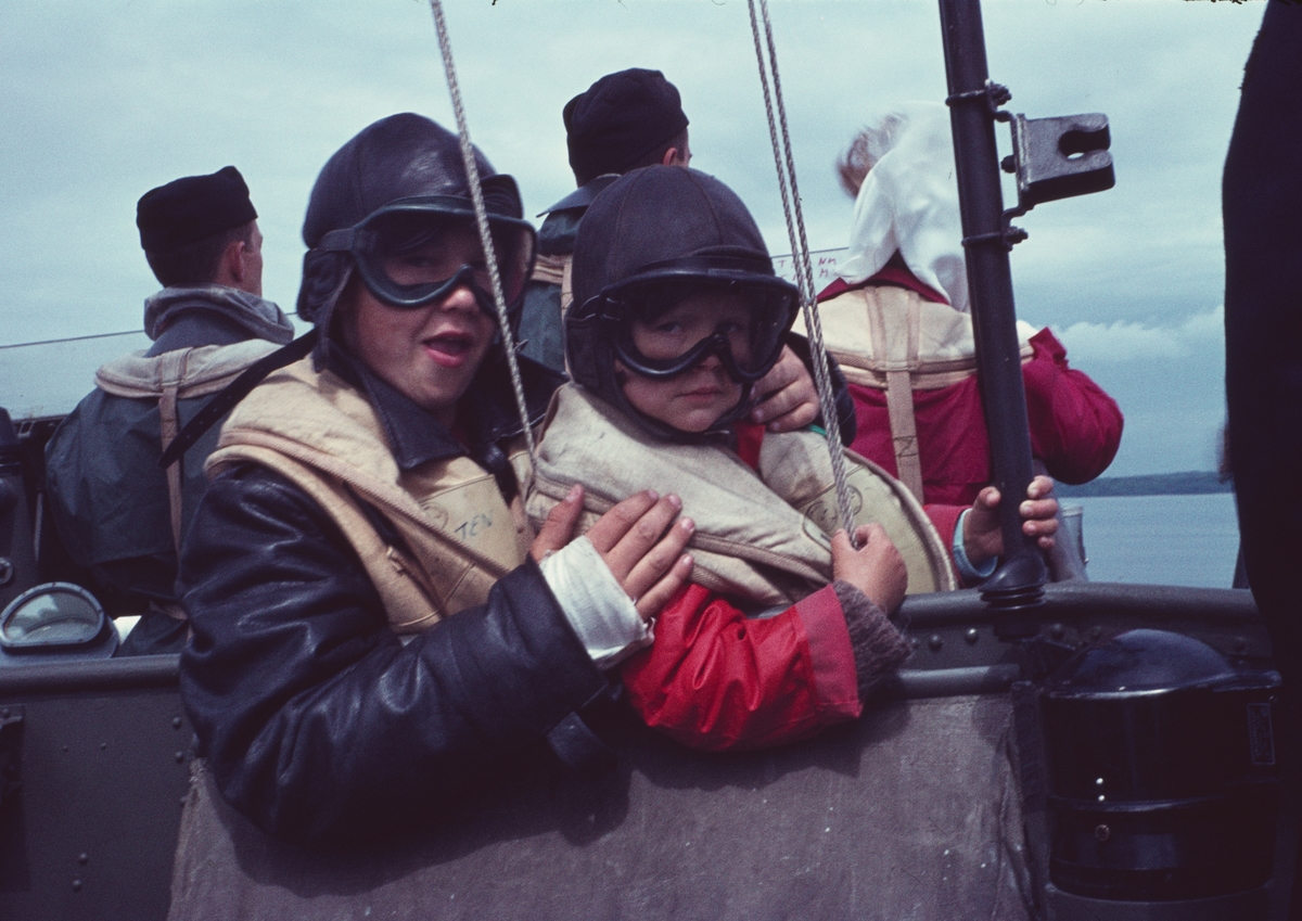 Bilden visar två barn i skyddkläder ombord på en motortorpedbåt.