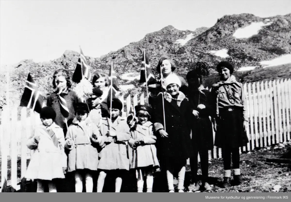 Honningsvåg, Holmbukt. Barn og voksne i finklær og med flagg. Til høyre to speiderjenter. 17. mai 1929 eller 1930.