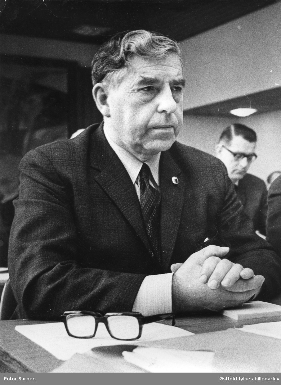 Portrett av gårdbruker Johan Volden (1912  -1979). Ordfører i Eidsberg fra 1951-1979, vararepresentant (1961-65) på Stortinget/Senterpartiet.  Person i brakgrunn er ukjent.