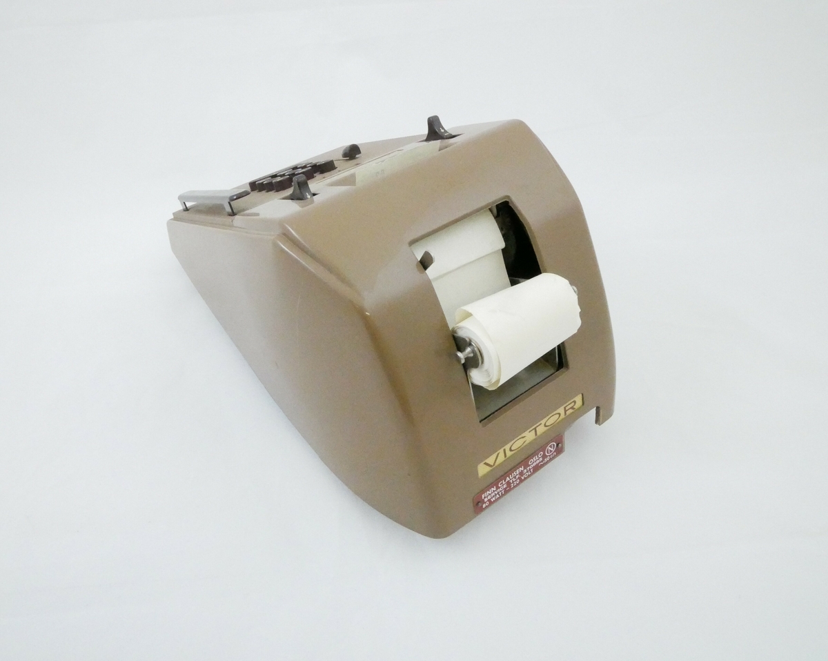 Elektrisk regnemaskin i brun hard plast. På forsiden er det et panel med brune knapper. Bak er det et rom hvor papir oppbevares, papiret trekkes inn i maskinen og ut på forsiden av maskinen. Nederst bak er det en ledning for strøm. 

Påskrift: 
[Foran på panelet]: VICTOR 
[Bak på maskinen]: FINN CLAUSEN OSLO // SERVICE TLF: 370995 // 80 WATT - 220 VOLT 
[Under på bunnen]: SER 1937 - 674 // MOD 7 83 54 // THIS MACHINE PROTECTED BY // U.S.A AND FOREIGN PATENTS // MADE BY VICTOR ADDING MACHINE CO. // CHICAGO U.S.A