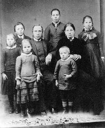 Gruppbild med familjen Karl Fredriksson i Skymmesås. Föräldrarna Karl och Gustava sitter intill varandra på stolar omgivna av sex barn.