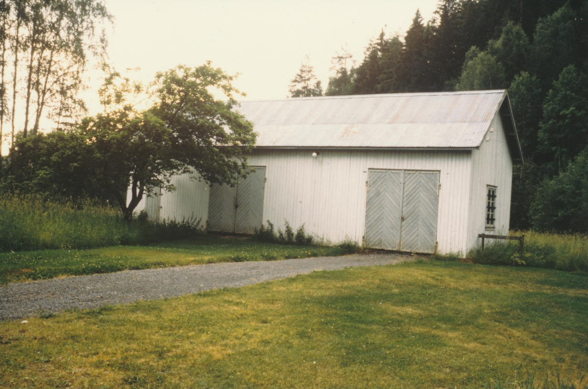 Vognskjulet på Kistefoss. Hvitmalt bygning med bølgeblikktak, to doble gråmalte porter og en liten grå dør inn til utedo helt til venstre.