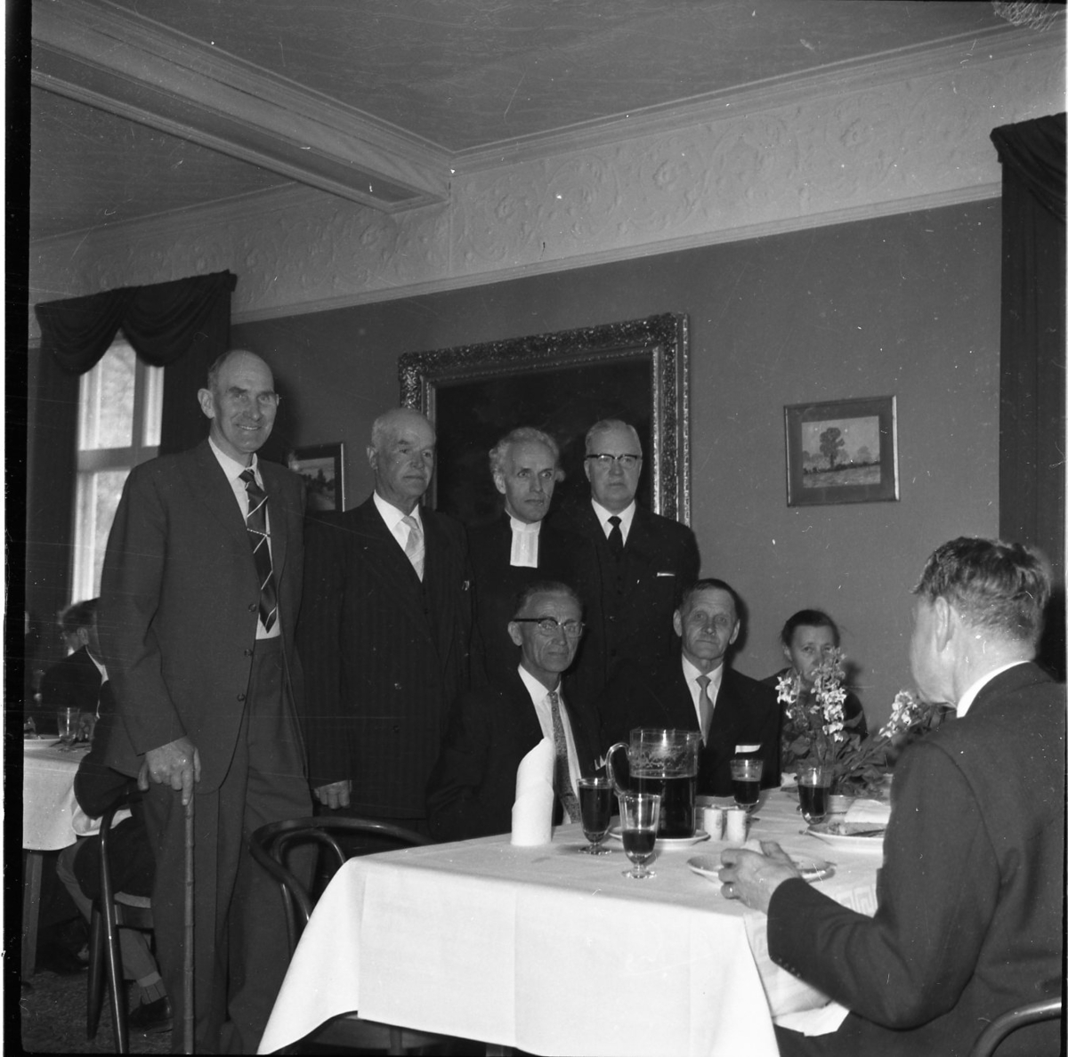 Konfirmandträff i St Hultrum. Fyra män står bakom ett dukat bord där andra män sitter och äter. Prästen som står som trea från vänster är Tore Lord. Någon av de andra är sannolikt Axel Wier.