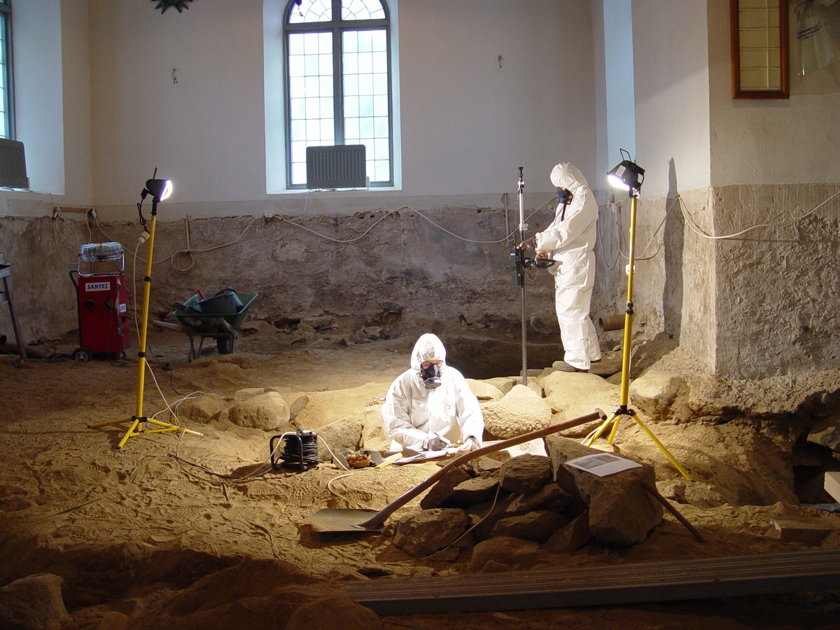 Interiör från Barnarps kyrka i Jönköpings kommun. Inför planerad ny golvläggning i samband med fukt- och mögelsanering genomfördes en arkeologisk undersökning i kyrkan under år 2006. På grund av den ohälsosamma arbetsmiljön bär arkeologerna på bilden skyddskläder.