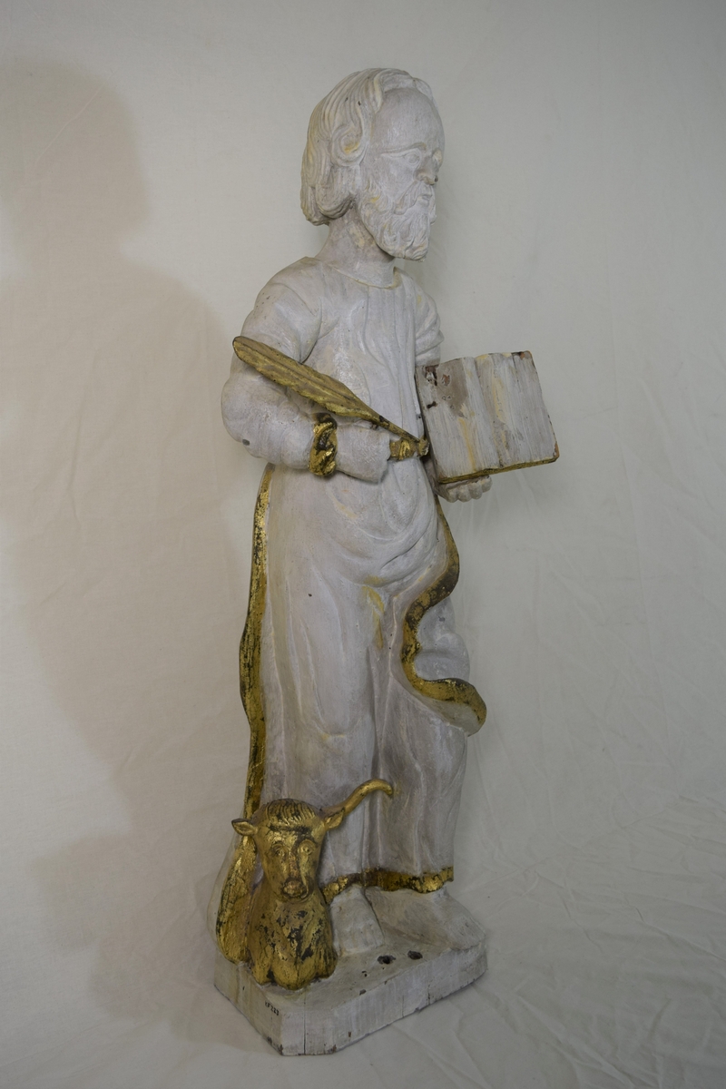 Evangelisten Lukas, støttet til høyre ben med oksens forkropp ved foten, oppstått bok på venstre hånd, flik av kappen inn over venstre lår.