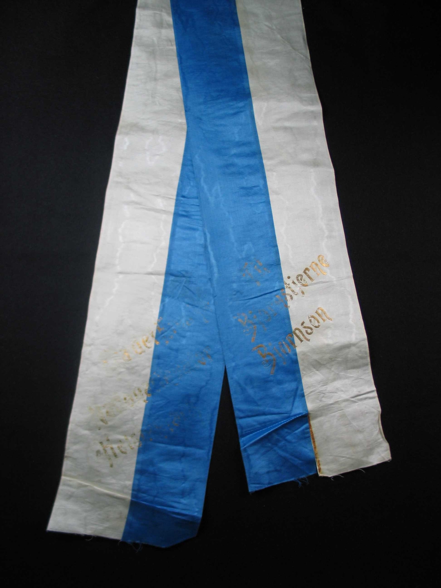 Begravelsessløyfe i hvit og blå silke med tekst i gull.