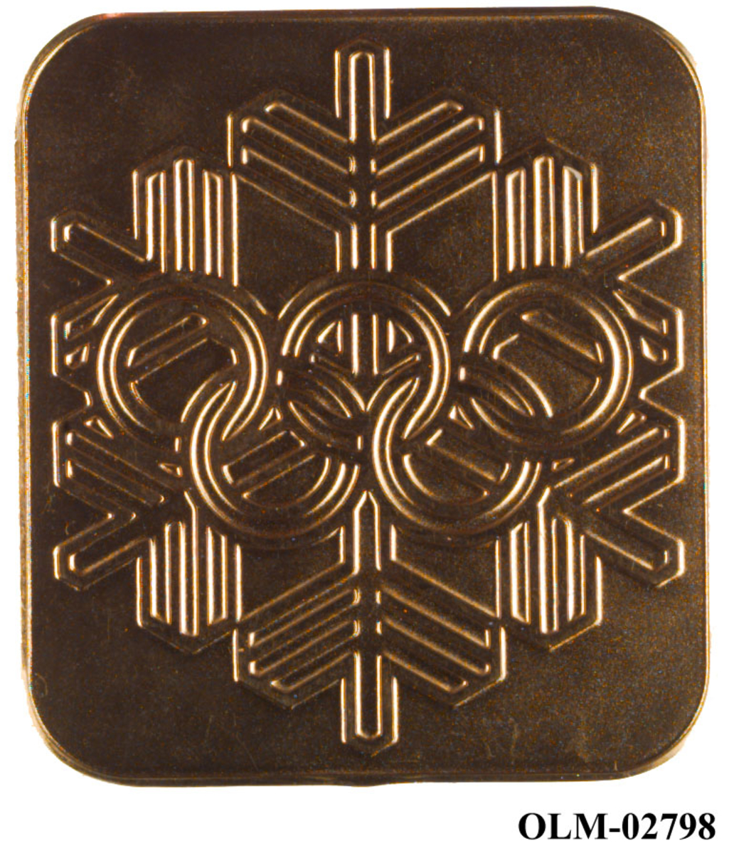 Gullfarget minnemedalje med motiv av en snøkrystall og de olympiske ringene.