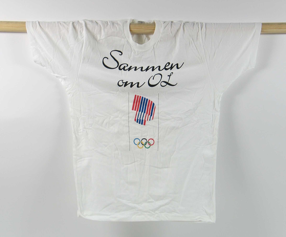 Hvit t-skjorte i størrelse medium. Påskriften "Sammen om OL" på fremsiden. På fremsiden er det også en logo for de olympiske vinterleker på Lillehammer i 1994.