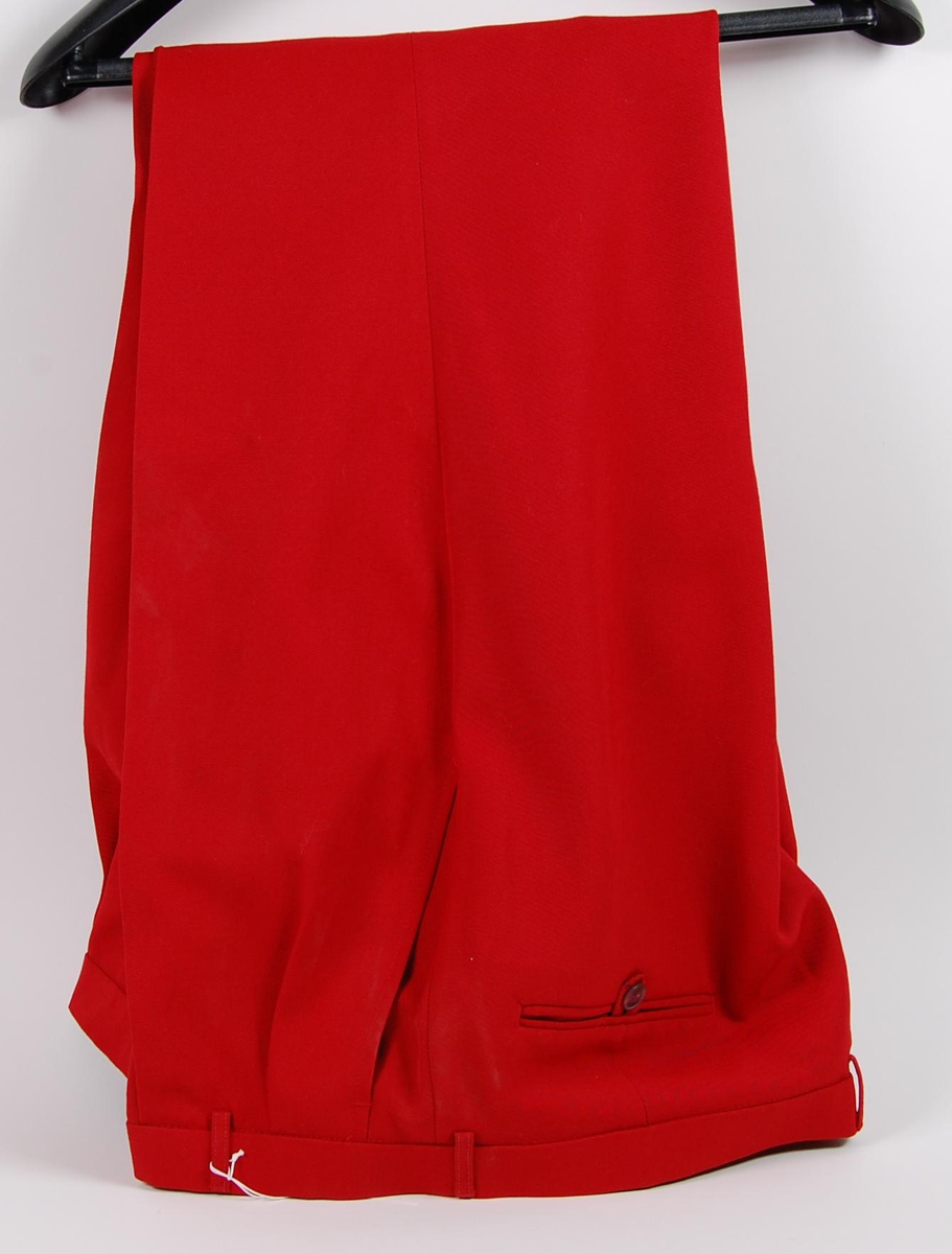 Rød dress bestående av jakke og bukse. På jakka er det påsydd et merke med de olympiske ringene, norske flagget og innskriften: NORGE. 