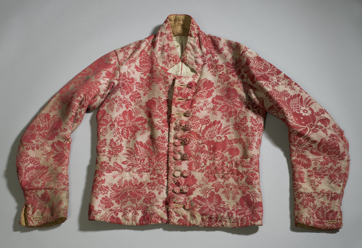 Håndsydd vest av ulldamask, fôret med to typer linstoff. Ryggsømmene er sydd med spilesøm. Vesten har ståkrage, dobbel knapphullrad (18) , trekte knapper (to ulike stoff) (16) - to mangler. Det vil si ni knapphull  og knapper på hvert forstykke. Knapphullene er sydd med lintråd.
To sidelommer. Knapp og knapphull nederst på ermene.