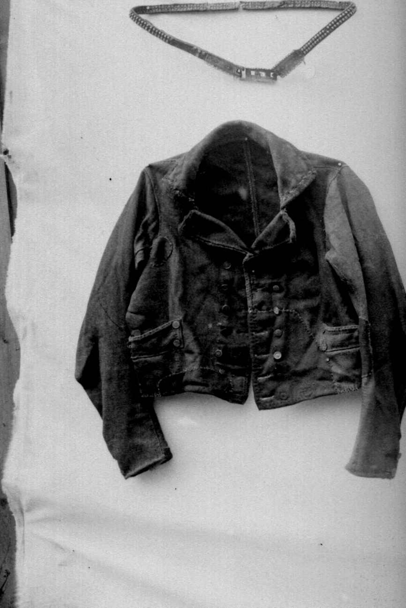 Trøye av kypertvevd vadmel. Ryggsøm og panelsømmer på hver side. Trange ermer. Høy oppstående linningskrage med plass for fire knapper på hver side - to mangler. Kragen har stikninger. Nedbrettet slag. Kragen og slagene er kantet med grønn plysj.
Knapphullsrad og knapperad (7, flere forskjellige motiv) på begge forstykkene slik at trøya kan kneppes både til høyre og venstre. 
Ermesplitt med to knapphull. En knapp mangler på venstre side. Knappene har nok opprinnelig vært festet med skinnsnorer og ullsnorer på vrangen.
En lomme på hvert forstykke, 5 knapper på hver. En lomme mangler fôr, en har ullfôr.
Spor etter fôr (?) på vrangen av forstykkene.  
Trøya har gjennomgått store reparasjoner.
