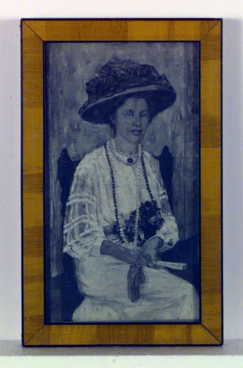 Portrett av sittende kvinne. Kvinnen er iført hvit kjole og stor hatt. Hun har blomster i fanget og lange kjeder rundt halsen.