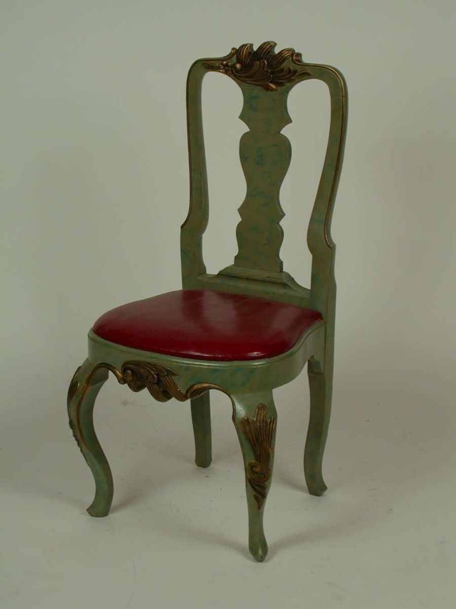 Lasert grønn stol med løst sete med polstring dekket med lær. Læret er rødt. Stolen har svungne forben med bronsert dekor på knærne. Stolen er dekorert med bronsert bladverk på sarg og toppstykke.