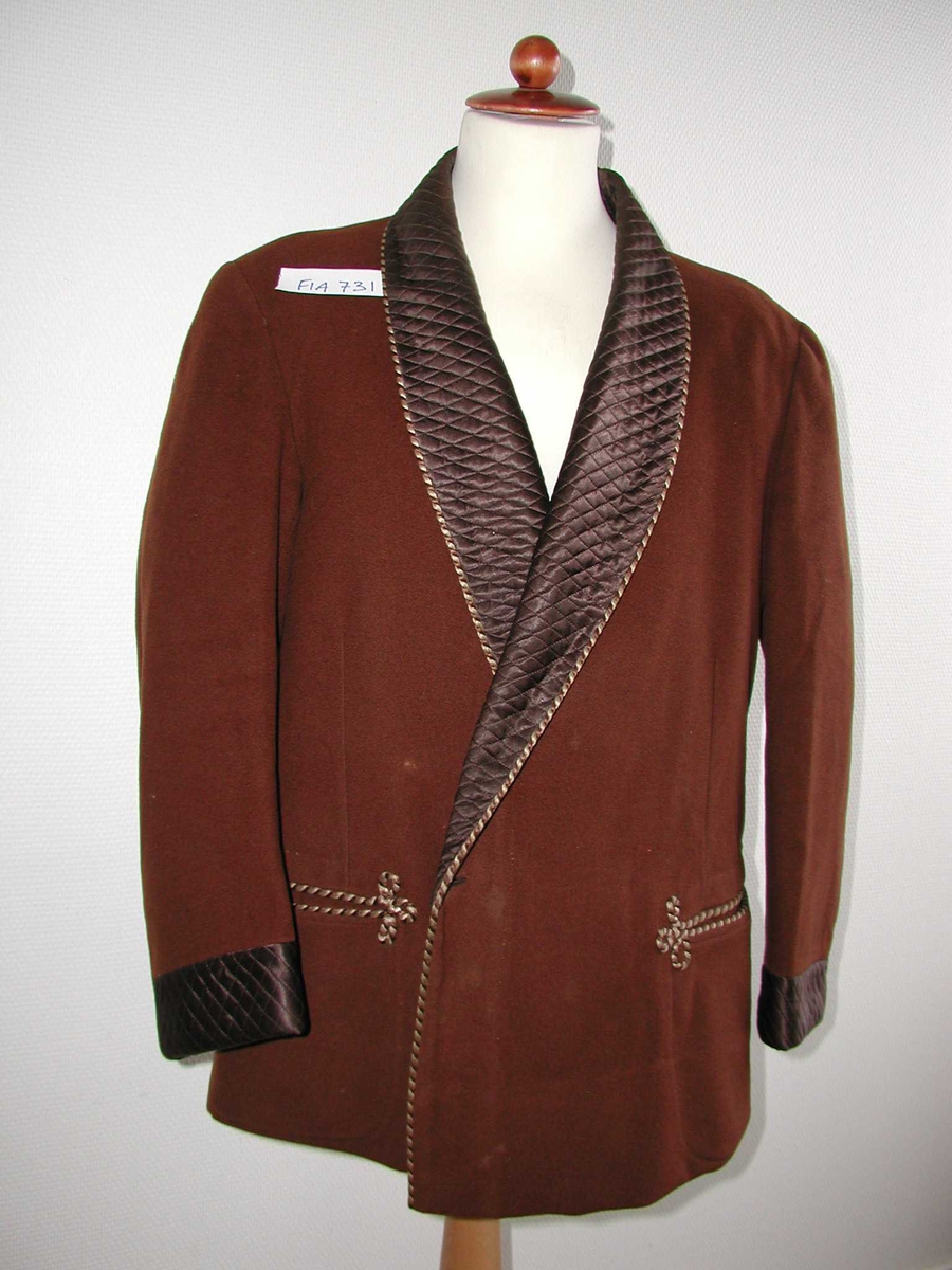 Ulljakke med vatterte silkeoppslag på krave og ermer. Snorer som dekor langs kanten og rundt lommene.