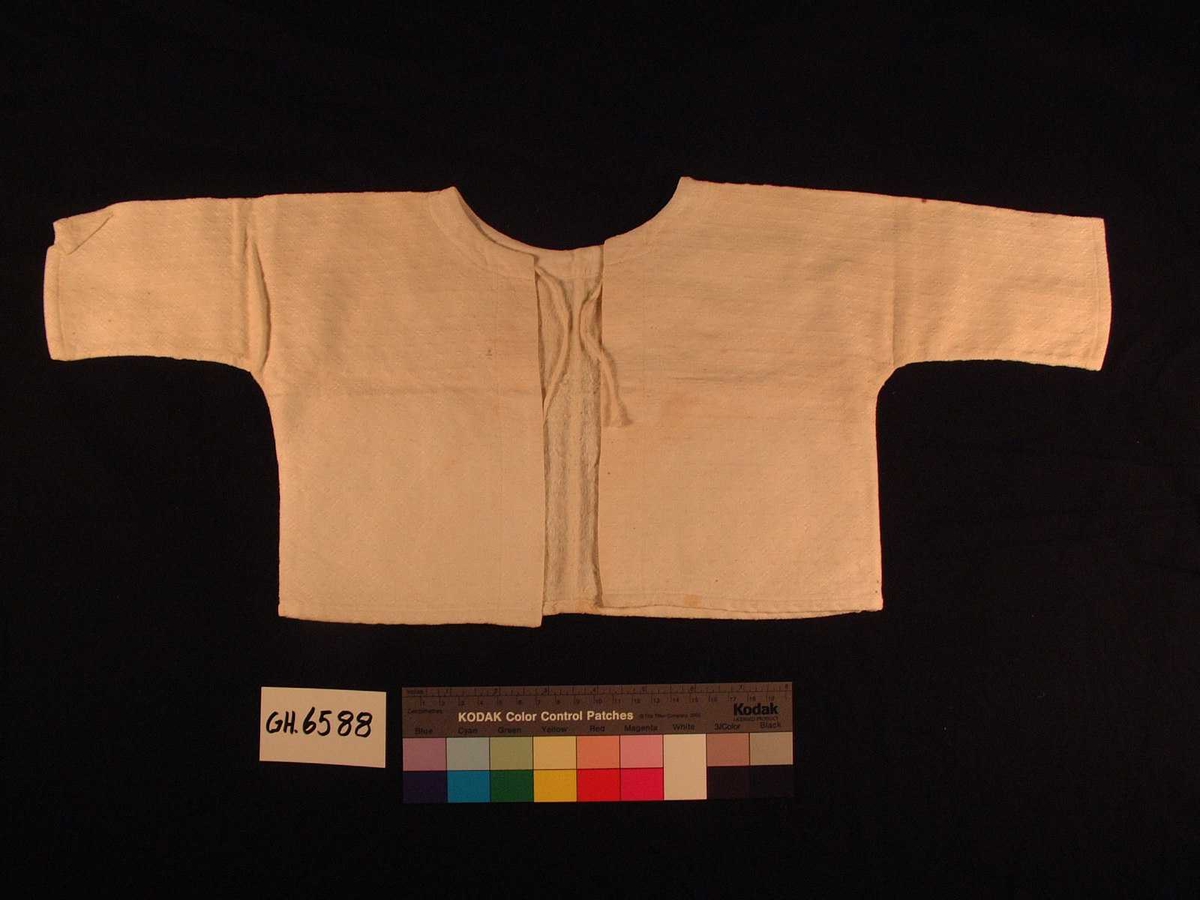 Skjorte til barn/spebarn i mønstervevd stoff.. Enkelt primærsnitt, lange ermer og åpning med knytebånd bak.