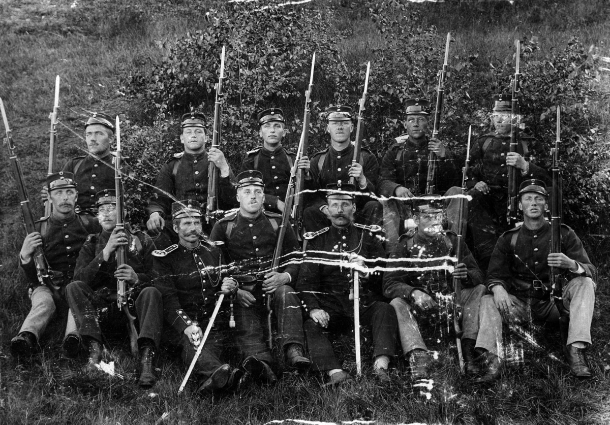 Gruppebilde. Soldater med gevær sittende i gresset.
