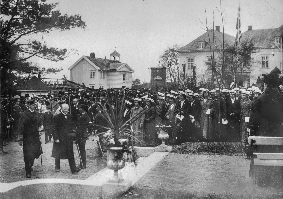 Utenfor Eidsvollbygningen 16. mai 1914. Prins Olav og dronning Maud var på Eidsvoll 16. mai og dro til Oslo på ettermiddagen. 
Til venstre kan vi se Kong Haakon, Prins Olav og ordfører i Eidsvoll Anders Venger.