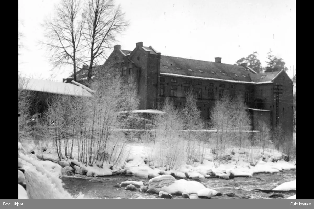 Akerselva rennende forbi fabrikksbygning tilhørende Nydalens Compagnie. Vinter