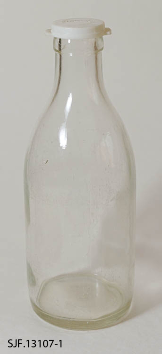 Melkeflaske bestående av flaske og lokk. Flaska er lagd av klart glass. Den er er 25,5 centimeter og har en sylindrisk kropp med 9,6 centimeters diameter. Cirka 14 centimeter ovenfor standflata skrår flaska slakt innover mot en krage rundt munningen. Her er diameteren (utvendig) 4,0 centimeter. I bunnen av flaska er det en del symboler i opphøyet relieff, blant annet noe som ser ut som en sammensmeltning av bokstavene «M» og «G» (som indikerer at dette er et produkt fra Moss Glassverk) samt «G» og «56». Flaska kan romme et væskevolum på 1 liter. Melk ble levert i slike flasker, med en foliekapsel over flaskemunningen. For å kunne lagre rester etter at foliekapselen var brutt hadde husholdningene gjerne en del plastdeksler som kunne gjenbrukes hver gang ei flaske med melkerester skulle settes til side i påvente av at resten av innholdet skulle konsumeres.  Denne flaska ble avlevert til museet med et kvitt plastdekksel med ordet «MELK» i opphøyet relieff på oversida. Dekselet er sirkelrundt, men har to utstikkende «ører» eller «flipper», plassert diameteralt overfor hverandre, som ble brukt når dekselet skulle løsnes.