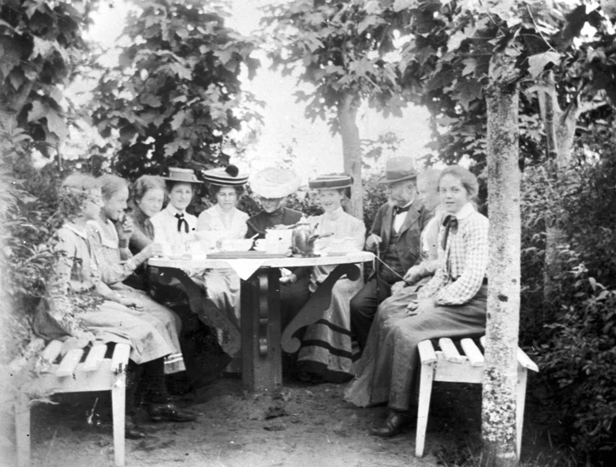 Gruppe damer og en mann rundt et kaffebord i hagen på Vesle-Ile, Furnes, Ringsaker.