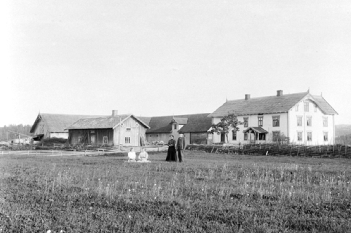 Eksteriør, gardsbruk, Soug østre, Ringsaker. Til venstre er Raubygningen, låve, hovedbygning. Personene i bildety er Agnethe og Ole Soug med døtrene Dagny og Aagot.
