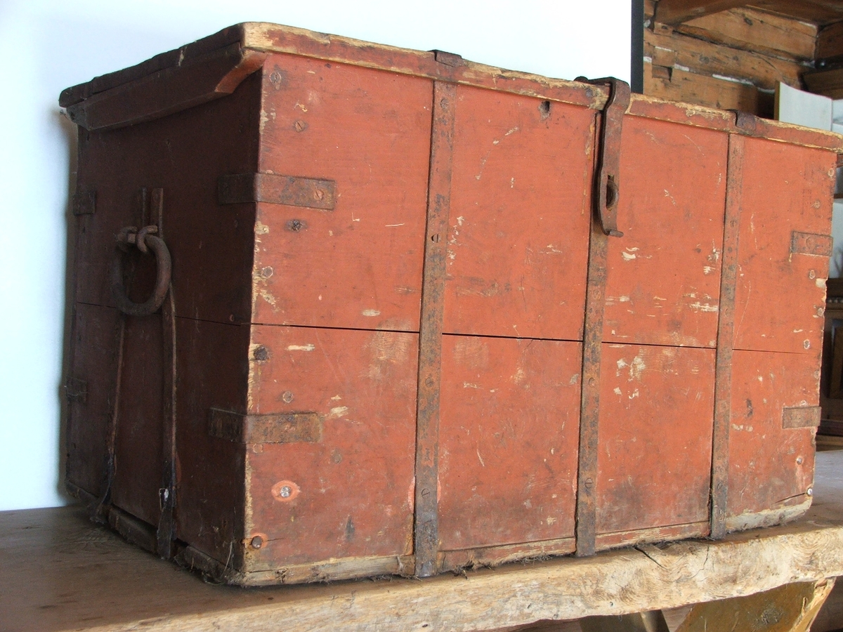 Rødbrun kiste med flatt lokk, handtak på sidene og 3 jernbeslag på lokk og framside. To jernbeslag på bakside. Kista har hengsel for lås. Kista består av ett rom.