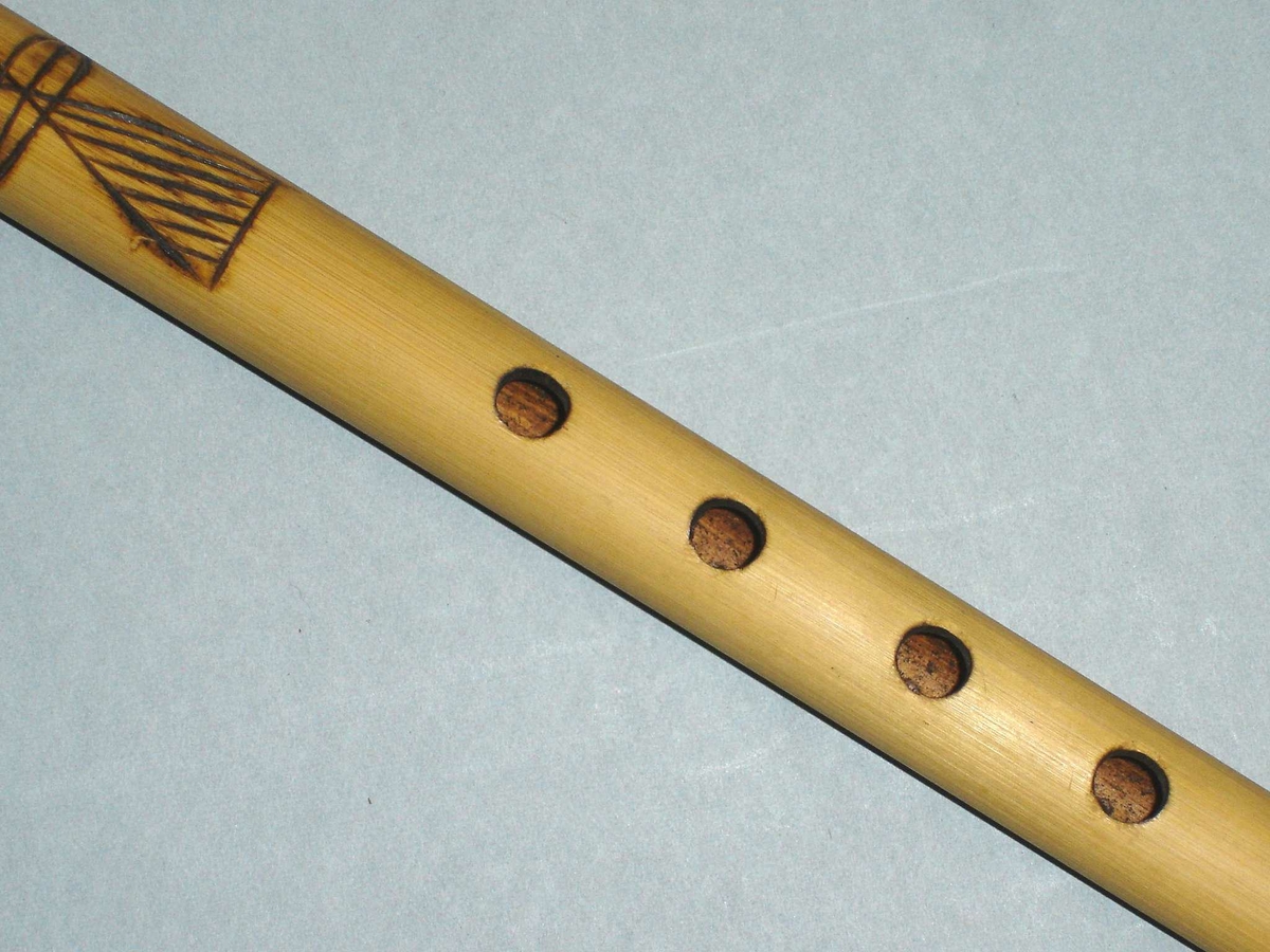 Fløyte i bambus med seks fingerhull og ett blåsehull. Innbrent dekor.
