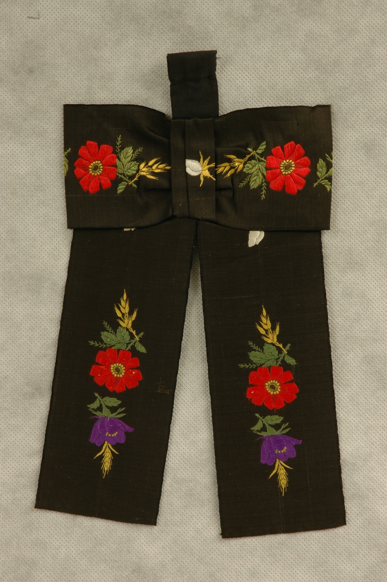 Hukkuband sydd av 7 cm bredt silkeband, svart i botn med mønster av brosjerte blomster i flere farger.