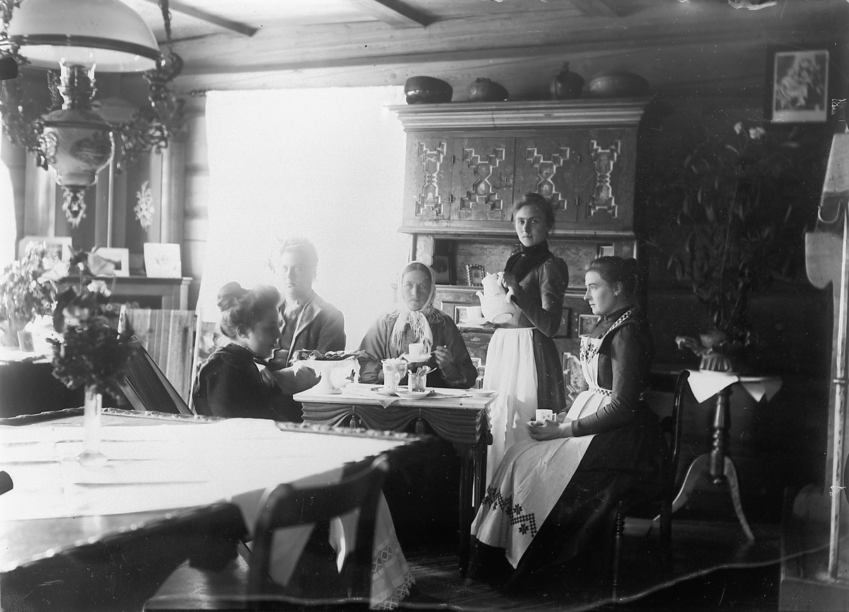 En gruppe kvinner og en mann drikker kaffe ved et stuebord. 