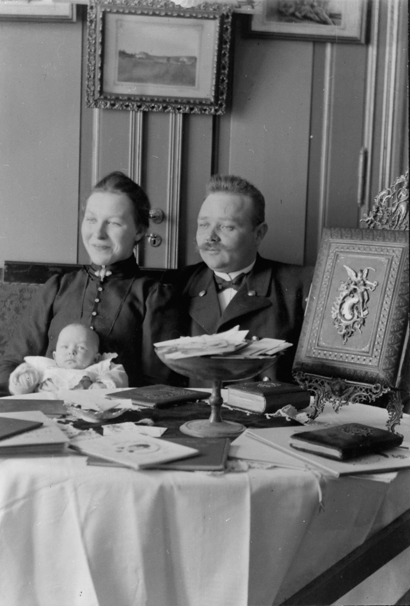 Familefoto, jernbaneuniform, Johanne Alhaug (1886-1979) og Johannes Alhaug (1873-1950) med datter Margit Alhaug (1904-), fotoalbum, visittkortalbum på bordet,