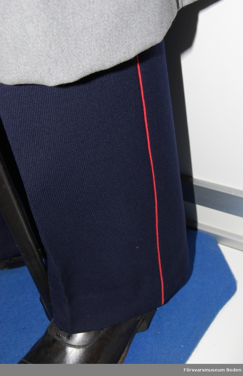 Mörkblått kläde med röda passpoaler längs yttersömmarna. Hällor monterade med dubbla knappar längst ner på byxbenens insidor.