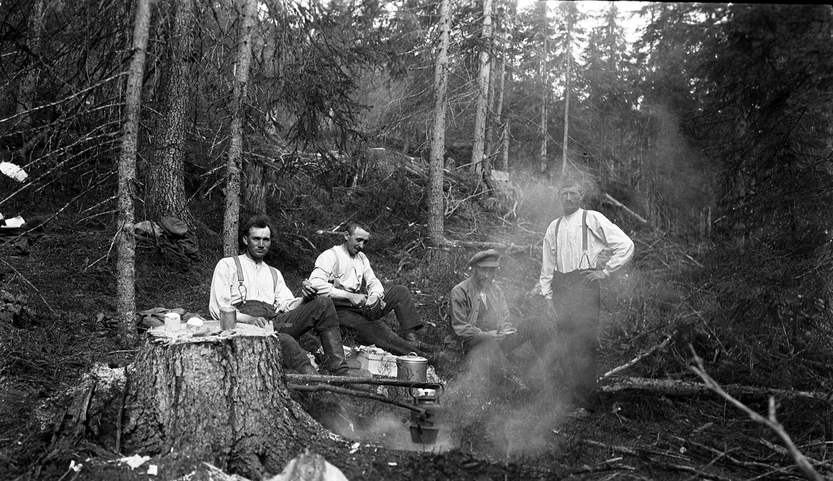 Fire menn ved kaffebål i skogsterreng. Fra venstre sitter Ole Natanael Gunnerød og Nils Gunnerød.  Stedet og de to øvrige personenes identitet er ukjent.