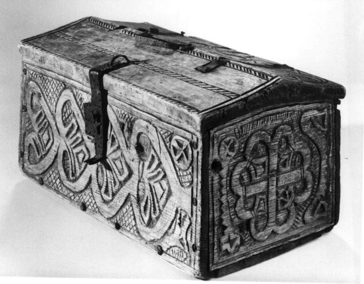 Skrin med flate sider of lett takformet lokk. Hengslet i bakkant og låsmekanisme i forkant. Håndtak midt på lokket. Hele utsidenhar skurd dekor med ranker, dyr og mennesker.