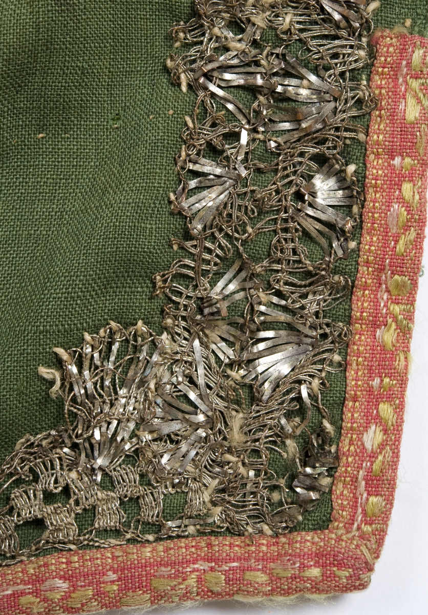 Grønt forkle av ull med dekor av metallblonder og bånd.