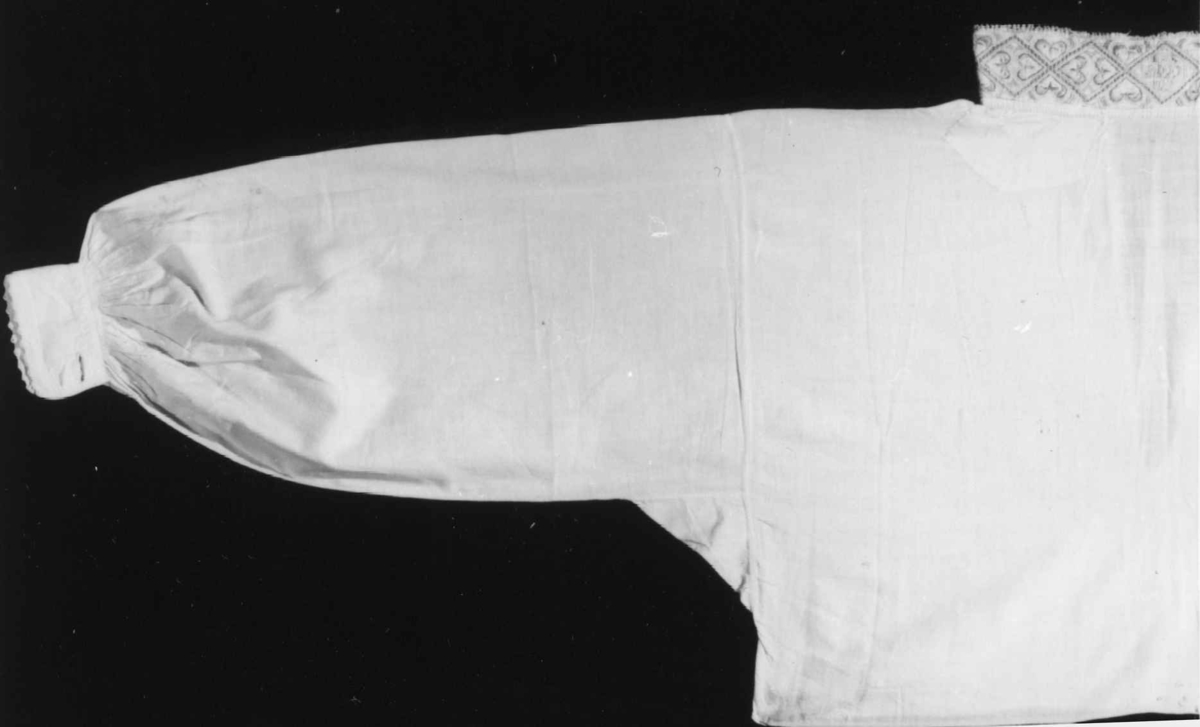 Skjorte brukt til belstestakk, kun broderi på halskvaren og hvite handkvarer med lite pynt. Sydd av tynt bomullsgarn.
Kvaren 6x41cm, senere forlenget framme med 2,5cm på hver side.