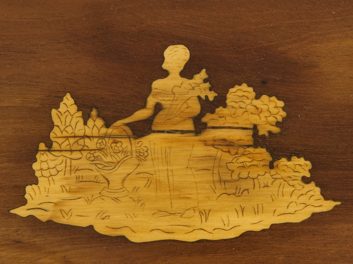 Rektangulært mahognibord med bordplaten som kan klaffes. På sarg og bordpalte båndintarsia, på platen intarsia med landskapsmotiv og figur. 
Innvendig et stykke lys ved med påskrevet: Den 17.de Junii 1819.