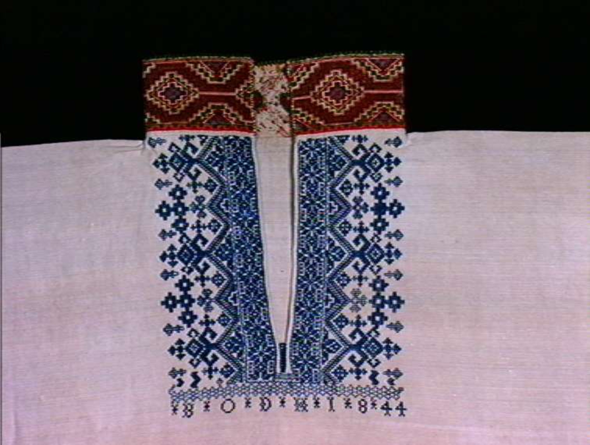 Hvit skjorte med blå brodert dekor i ermslut og hals, en flerfarget krage.