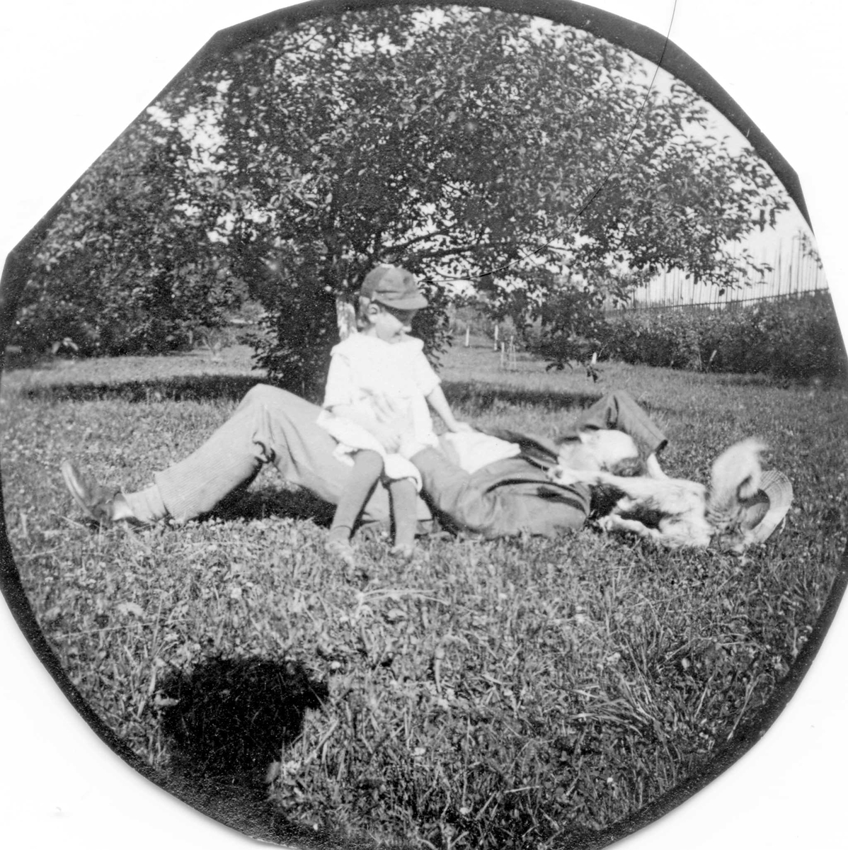 Dr. Elling Holst ligger i gresset med datteren Aagot på fanget, hund liggende ved siden av.